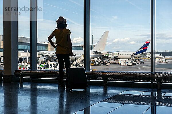 Silhouette einer Frau mit einem Koffer im Flughafenterminal mit Blick auf die Flugzeuge warten auf den Flug