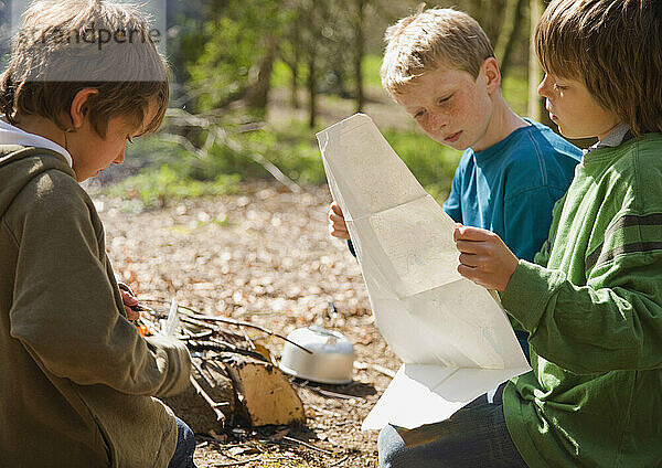 Drei Jungen knien am Lagerfeuer und schauen auf die Karte