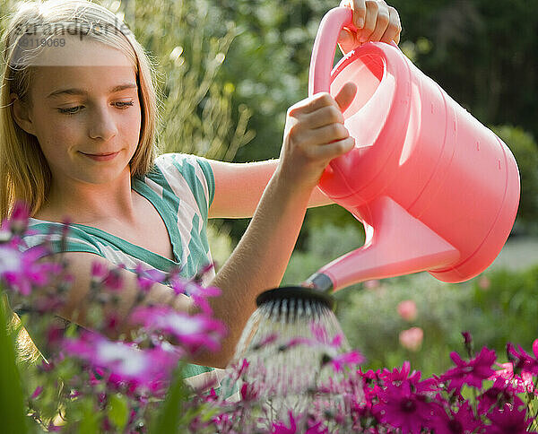 Porträt eines jungen Mädchens  das Blumen mit einer rosa Gießkanne gießt