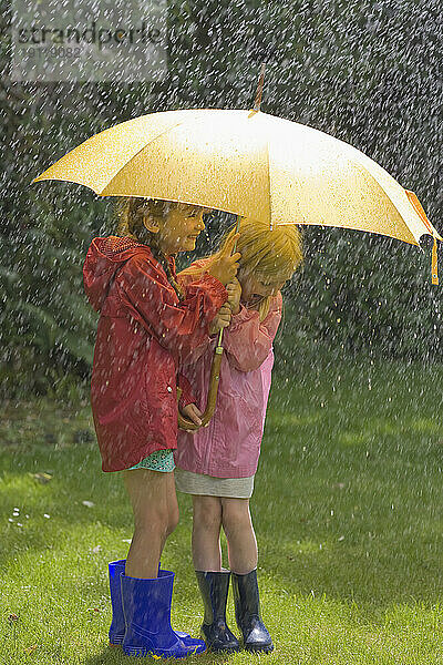 Zwei junge Mädchen im Regen unter gelbem Regenschirm