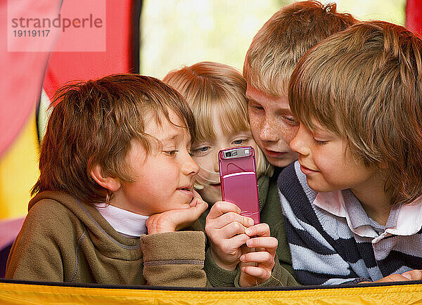 Porträt von Kindern  die in einem Zelt liegen und Textnachrichten auf einem Mobiltelefon senden