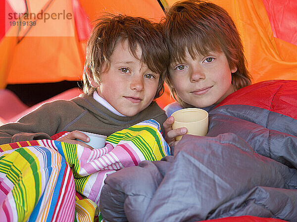 Porträt zweier Jungen  die in Schlafsäcken in einem Zelt sitzen
