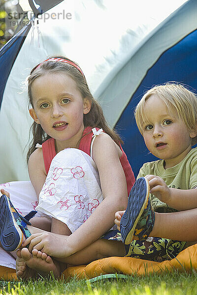 Porträt eines Jungen und eines Mädchens  die am Zelt sitzen
