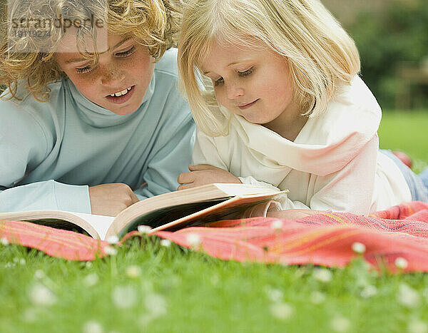 Zwei Kinder liegen im Garten und lesen ein Buch