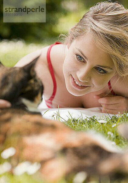 Junge Frau liegt im Gras und streichelt eine Katze
