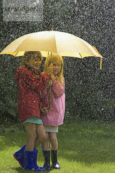 Zwei junge Mädchen im Regen unter gelbem Regenschirm