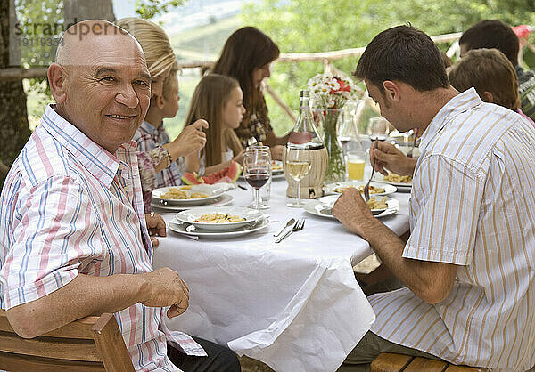 Großfamilie sitzt am Tisch und isst Pasta  im Vordergrund Opa