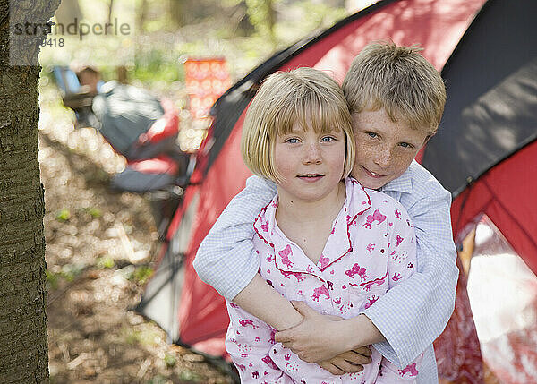 Porträt eines Jungen und eines Mädchens  die sich vor dem Zelt auf dem Campingplatz umarmen