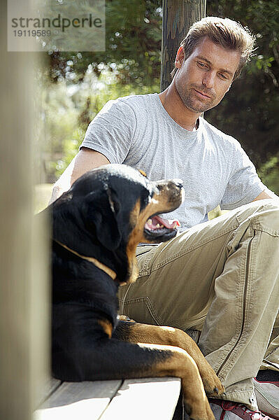 Mann sitzt mit seinem Hund unter der Veranda