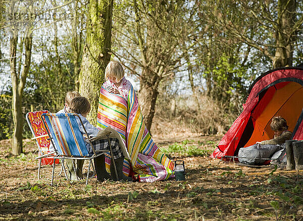 Junges Mädchen  in eine Decke gehüllt  interagiert mit Freunden auf dem Campingplatz