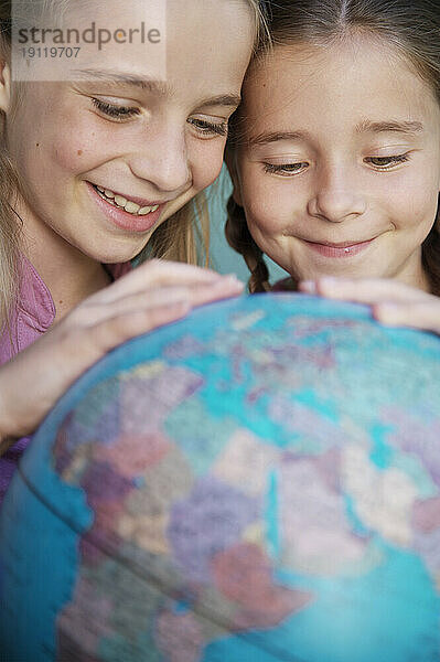 Zwei junge Mädchen berühren und drehen eine Weltkugel