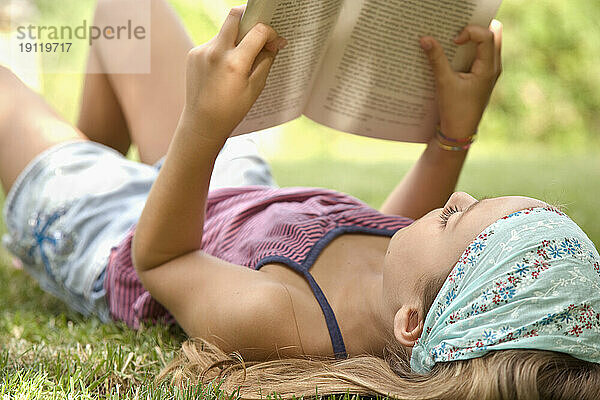 Porträt eines jungen Mädchens  das auf dem Rücken liegt und ein Buch liest