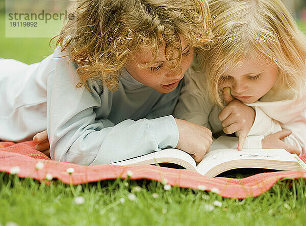 Zwei Kinder liegen im Garten und lesen ein Buch