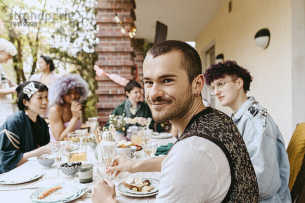 Porträt eines lächelnden schwulen Mannes  der mit LGBTQ-Freunden bei einer Dinnerparty im Hinterhof sitzt