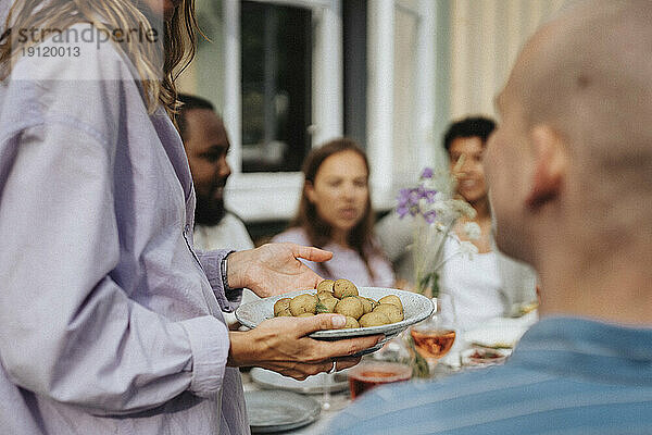 Mittelteil einer Frau  die während einer Dinnerparty im Café Babykartoffeln in Tellern hält