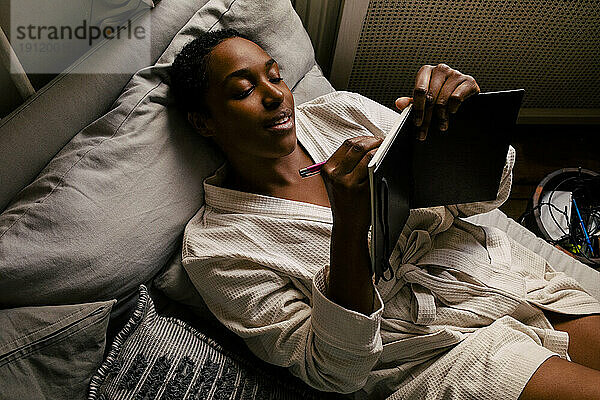 Hochformatige Ansicht einer Frau  die auf dem Bett liegend in ein Buch schreibt