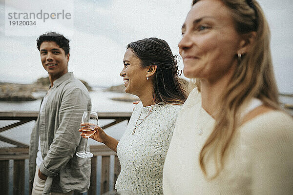 Glückliche Frau mit Wein in der Hand beim Spaziergang mit Freunden auf einer Brücke