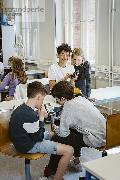 Männliche und weibliche Schüler benutzen Smartphones  während sie am Schreibtisch im Klassenzimmer sitzen