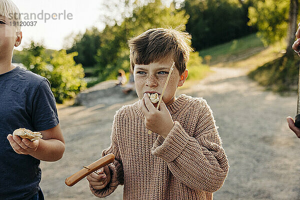 Junge trägt Pullover und isst Würstchen mit einem Freund im Ferienlager