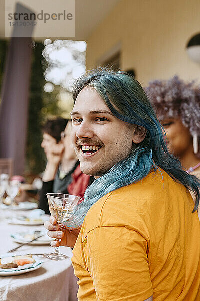 Porträt eines fröhlichen schwulen Mannes mit gefärbten Haaren  der sich mit Freunden bei einer Dinnerparty im Hinterhof vergnügt