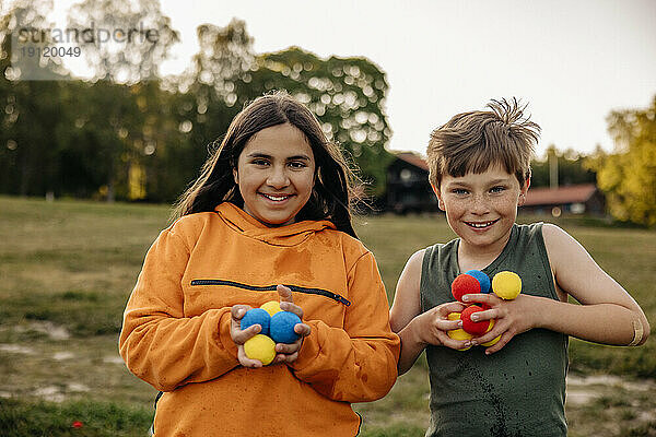 Porträt von glücklichen männlichen und weiblichen Freunden  die bunte Bälle auf einem Spielplatz im Ferienlager halten