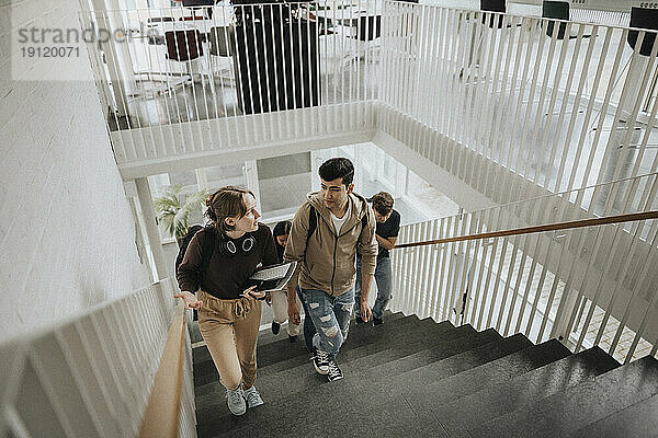 Hochformatige Ansicht von Studenten  die sich unterhalten  während sie eine Treppe in der Universität hinaufsteigen