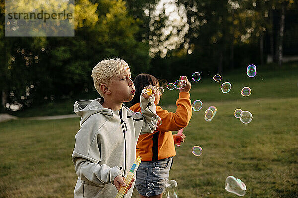 Junge bläst Seifenblasen mit einer Freundin auf einem Spielplatz im Ferienlager