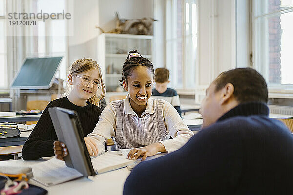 Lächelndes Schulmädchen zeigt einem männlichen Lehrer im Klassenzimmer einen Tablet-PC