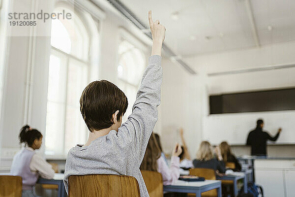 Junge hebt die Hand  während er eine Vorlesung im Klassenzimmer besucht