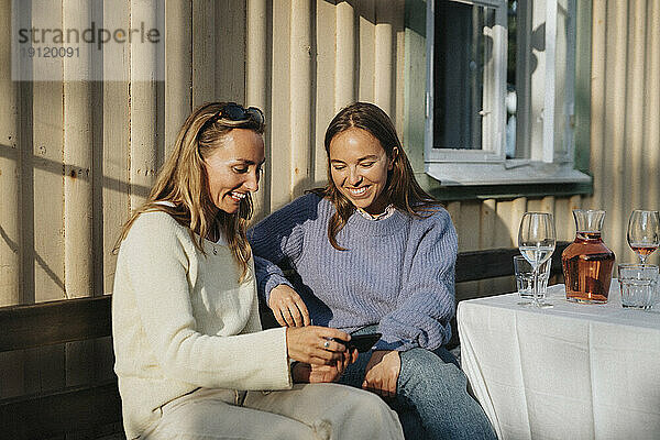 Glückliche junge Frau  die ihr Smartphone mit einer Freundin während einer Dinnerparty im Café teilt