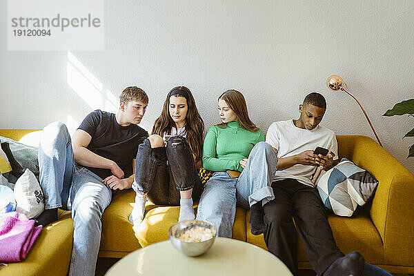 Junge multirassische Freunde benutzen Smartphones  während sie zu Hause auf dem Sofa sitzen