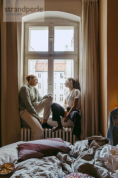 Junge Freundinnen unterhalten sich  während sie im Schlafzimmer am Fenster sitzen