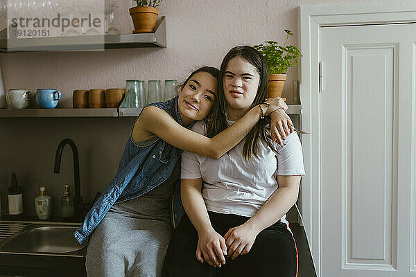 Junge Frau umarmt Schwester mit Down-Syndrom in der Küche zu Hause