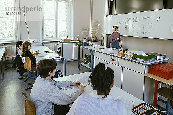 Lächelnde Lehrerin unterrichtet Schüler am Schreibtisch sitzend im Klassenzimmer