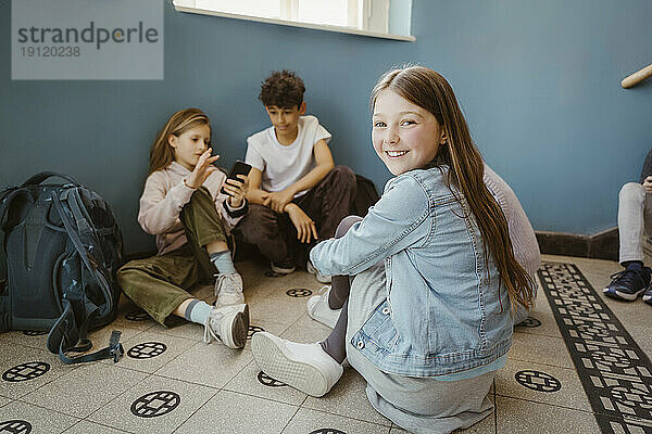 Porträt eines lächelnden Mädchens  das mit Freunden in der Schule auf dem Boden sitzt