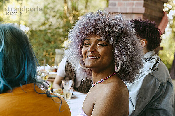 Seitenansicht Porträt einer lächelnden Transfrau mit lockigem Haar während einer Dinnerparty im Hinterhof