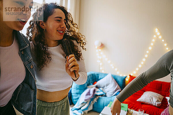 Frau hält Haarbürste und singt mit Teenager-Freundin zu Hause