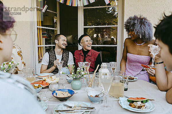 Glückliche LGBTQ-Freunde  die sich bei einer Dinnerparty im Hinterhof am Tisch unterhalten