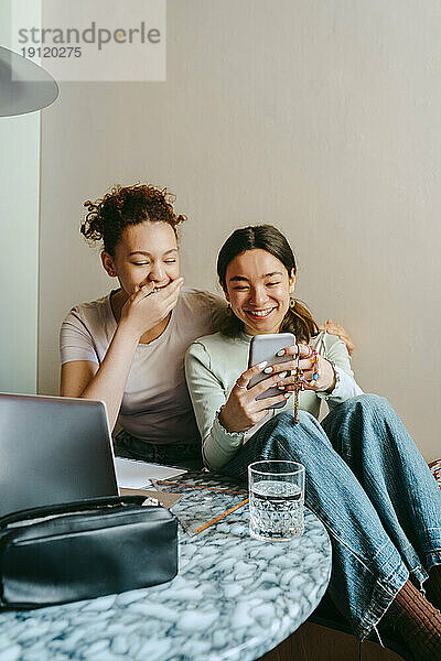 Glückliche junge Frau  die ihr Smartphone mit einer Freundin im Teenageralter teilt