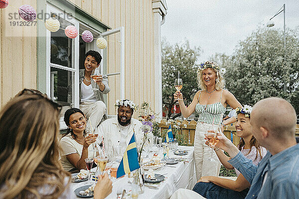 Glückliche männliche und weibliche Freunde stoßen mit Wein während einer Dinnerparty im Café an