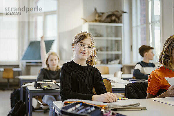 Porträt einer lächelnden Schülerin  die mit einer Freundin im Klassenzimmer am Schreibtisch sitzt