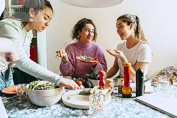 Frau serviert Mittagessen  während sich Freundinnen zu Hause unterhalten