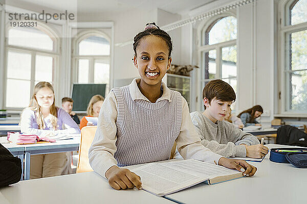 Porträt einer glücklichen Schülerin  die mit einem männlichen Freund im Klassenzimmer am Schreibtisch sitzt