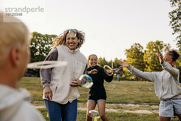 Fröhliche Kinder spielen inmitten von Seifenblasen mit einem Betreuer auf dem Spielplatz eines Ferienlagers