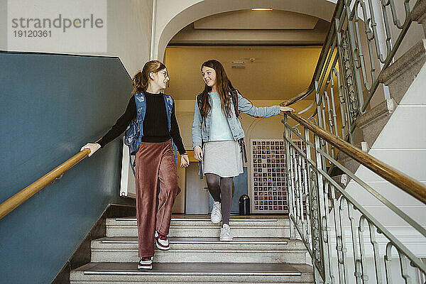 Lächelnde Freundinnen  die von einer Treppe im Schulgebäude heruntergehen