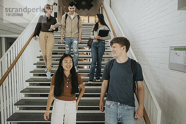 Glückliche multirassische Studenten  die sich unterhalten  während sie die Treppe in der Universität hinuntergehen