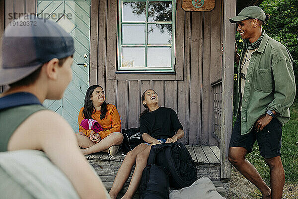 Mädchen lachen  während sie sich mit einem Betreuer unterhalten  der bei einer Hütte im Ferienlager steht