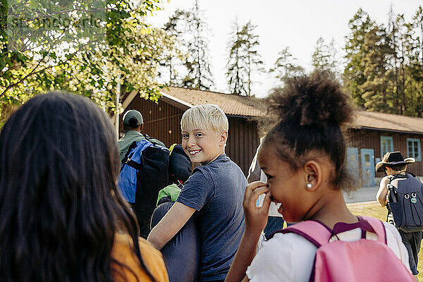 Porträt eines lächelnden Jungen  der über die Schulter schaut  während er mit Freunden im Ferienlager spazieren geht