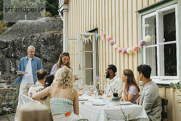 Lächelnde Frau serviert Essen an männliche und weibliche Freunde während einer Dinnerparty im Café