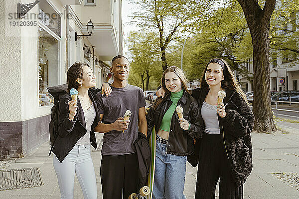 Porträt von lächelnden jungen Freunden  die am Straßenrand Eis essen